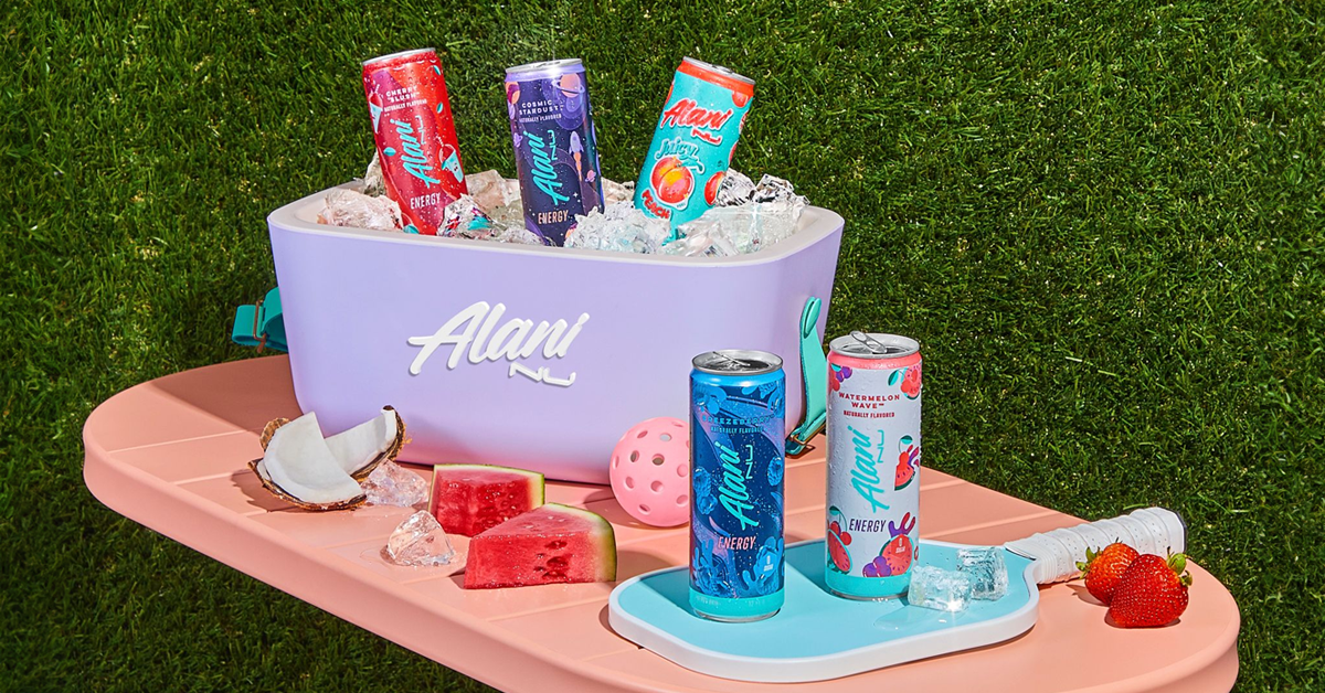 Alani Nu cooler full of energy drink cans on grass with watermelon and coconut